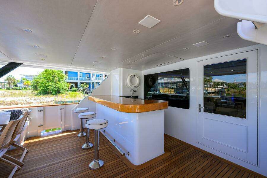 Outdoor bar area on 1997 Broward 108 Raised Pilothouse yacht with stools and wooden deck.