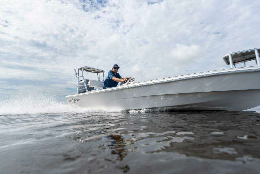 2025 BlueZones Boatworks 16' Flats boat speeding on water under cloudy sky.