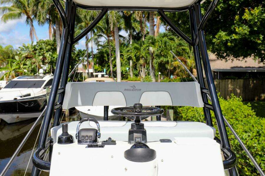 2020 Regulator 41 boat helm with steering wheel and controls, docked near lush greenery.