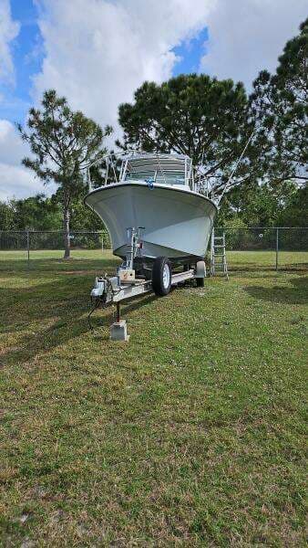 1988 Grady-White 25 SAILFISH boat on trailer, parked on grass, surrounded by trees.