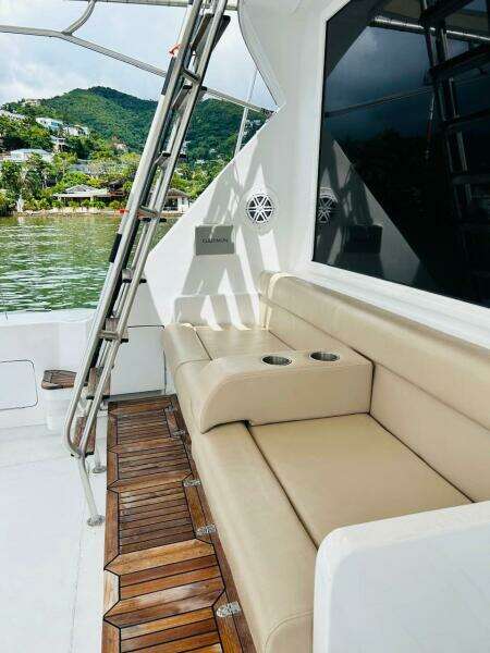 1988 Bertram 54' yacht with beige seating and wooden deck, docked by lush green hills.