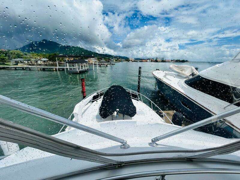 1988 Bertram 54' yacht docked in scenic marina, viewed through rain-speckled window.