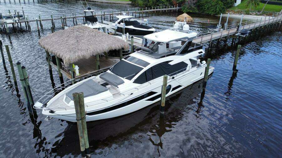 2024 Aicon 66 Vivere yacht docked at a marina with thatched roof hut.