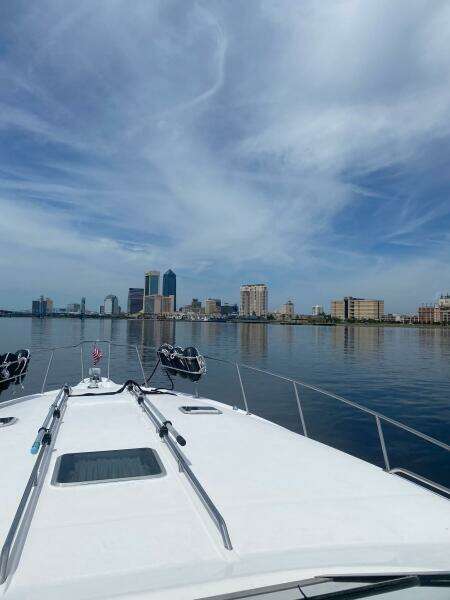 1993 Sea Ray 440 Sundancer cruising towards city skyline under blue sky.