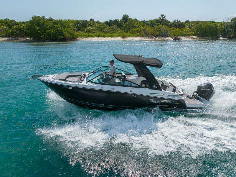 2023 Monterey 255 Super Sport boat cruising on clear blue water near a lush shoreline.