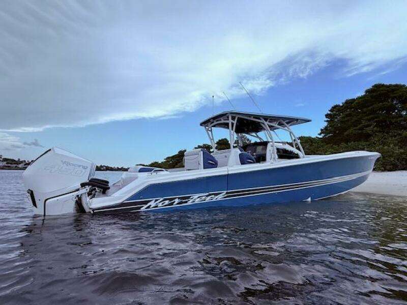 2022 Nor-Tech 390 Sport Center Console boat on calm water near a sandy shore.