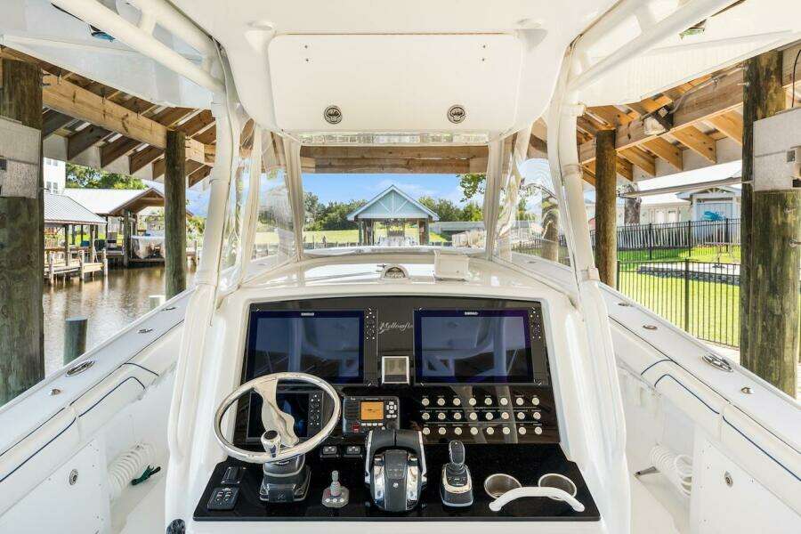 2015 Yellowfin 39 boat cockpit with advanced navigation controls, docked under a wooden shelter.