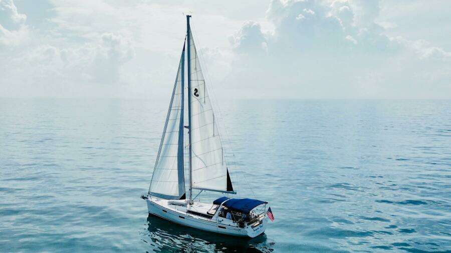 Sailing yacht Beneteau Oceanis 45, 2015 model, on calm ocean waters under cloudy sky.